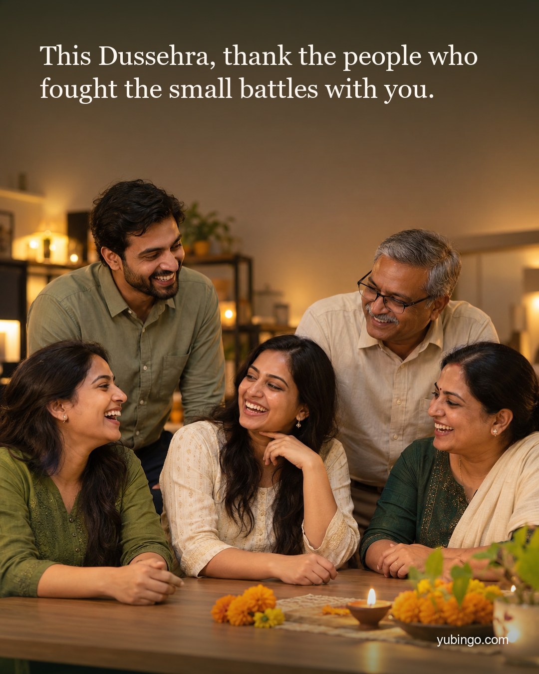 A small team of five laughing together around a desk in warm evening light, with marigolds and a lit diya. Text: This Dussehra, thank the people who fought the small battles with you.
